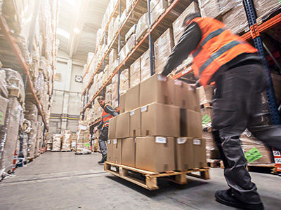 warehouse worker in orange safety vest pushing a pallet of boxes