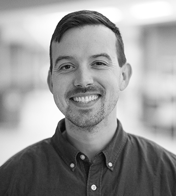 Black and white photo of a smiling man with a mustache, in a dark button up shirt